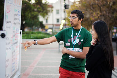 Student at Berkeley Project Day pointing at white board with project information while another student listens